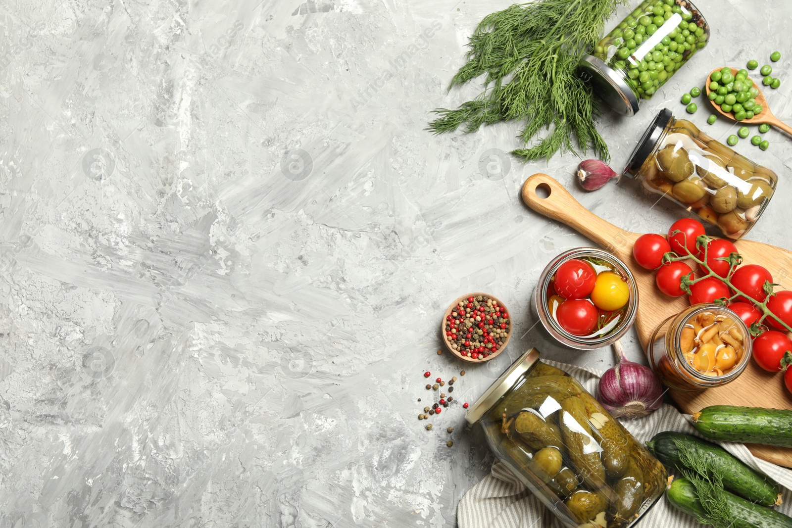 Photo of Different pickled products in jars and fresh ingredients on grey table, flat lay. Space for text