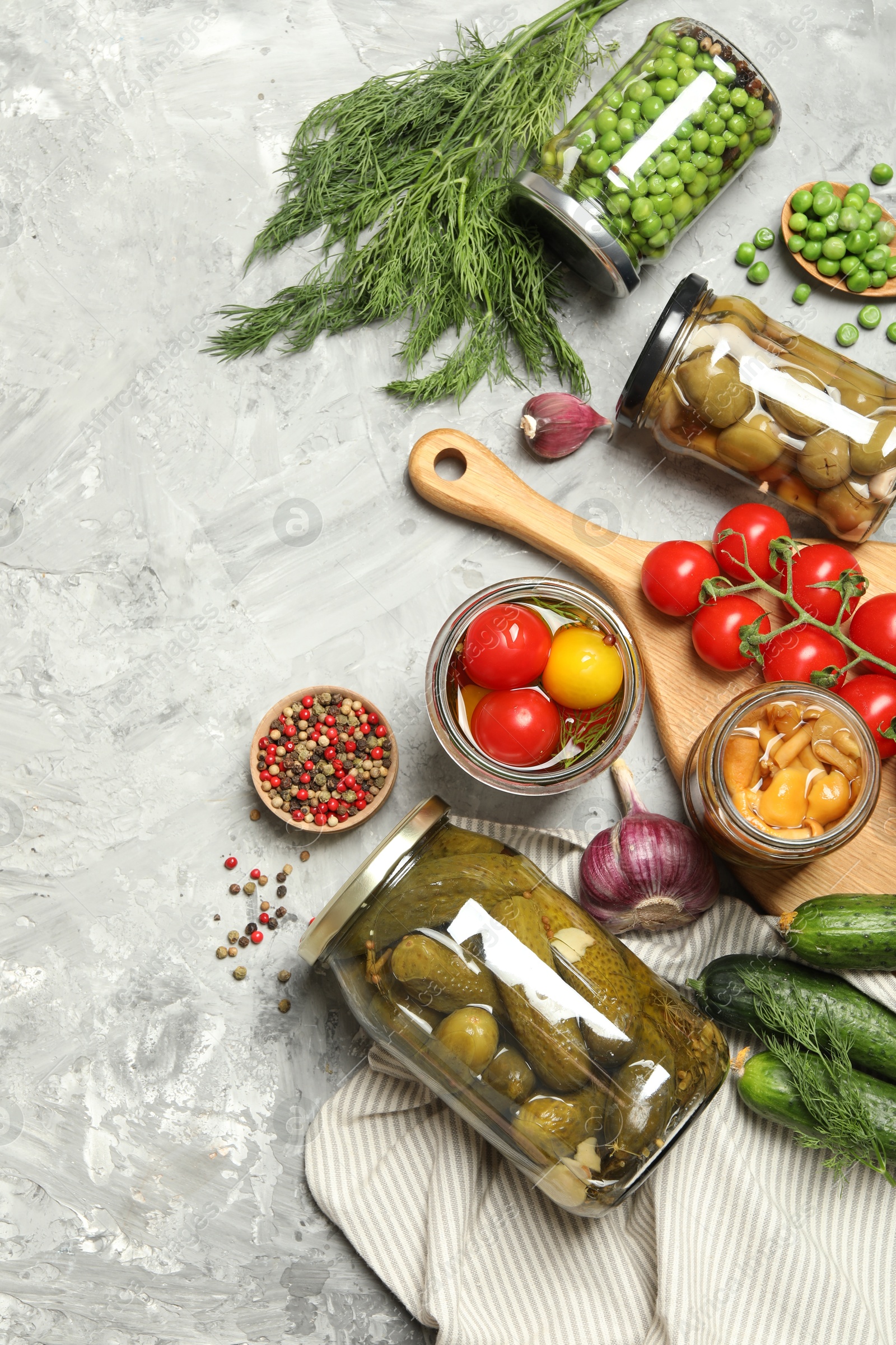 Photo of Different pickled products in jars and fresh ingredients on grey table, flat lay