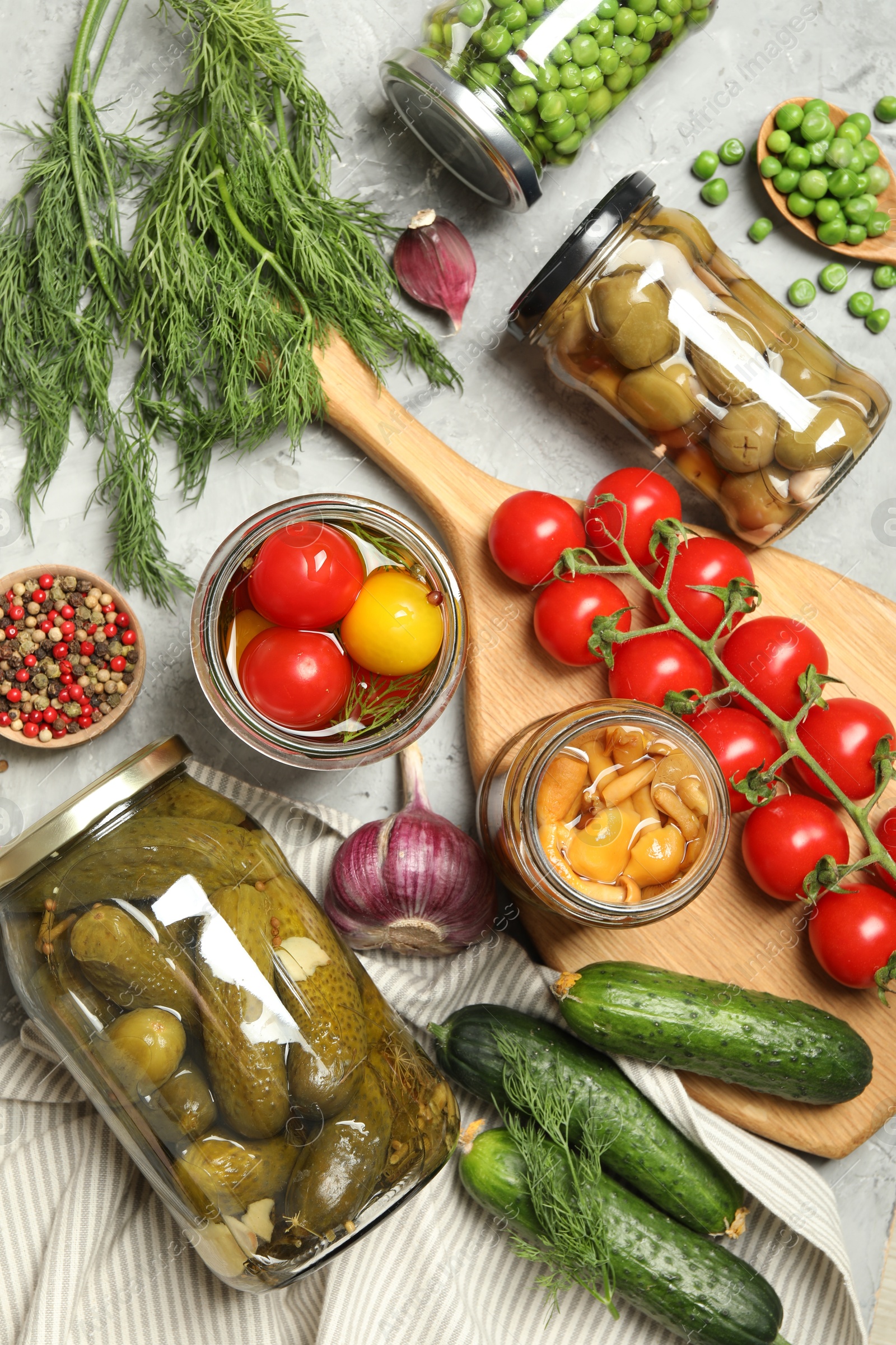 Photo of Different pickled products in jars and fresh ingredients on grey table, flat lay