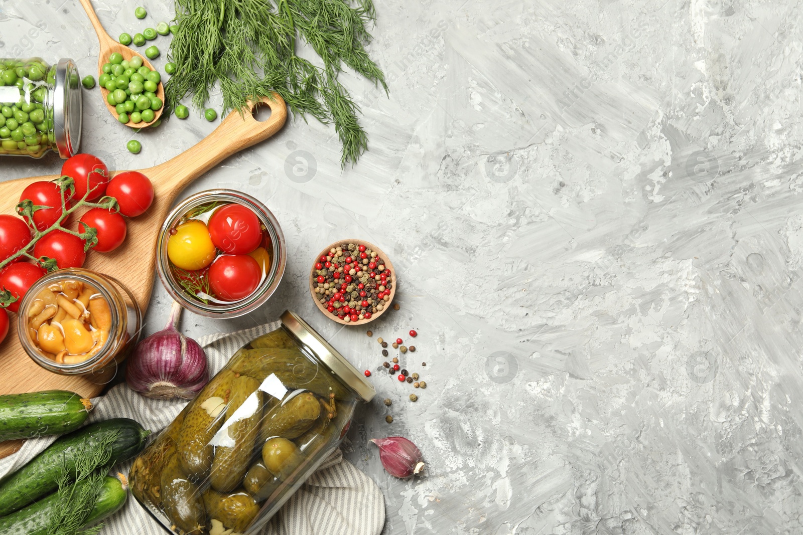 Photo of Different pickled products in jars and fresh ingredients on grey table, flat lay. Space for text