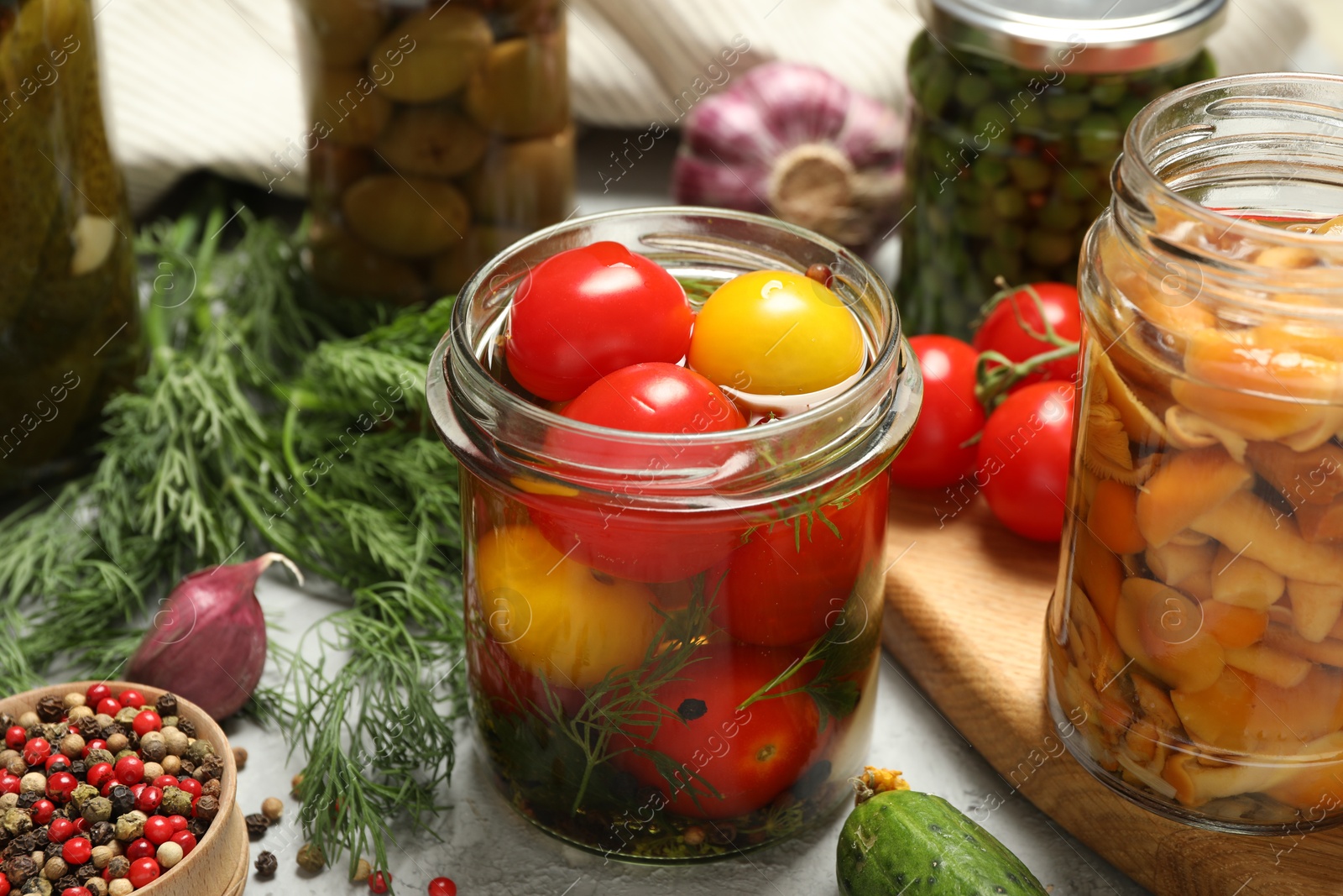 Photo of Different pickled products in jars and fresh ingredients on grey table, closeup