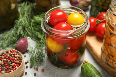 Photo of Tasty pickled tomatoes in jar and fresh ingredients on grey table, closeup