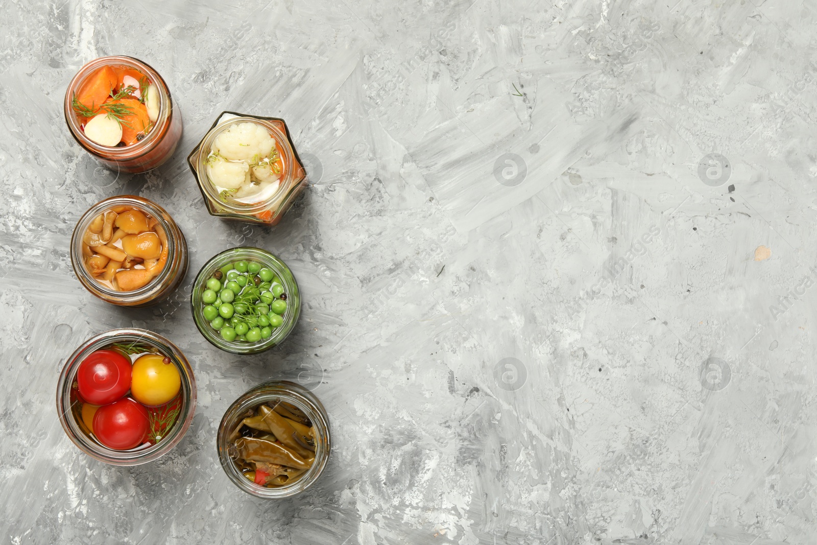 Photo of Different pickled products in jars on grey table, flat lay. Space for text