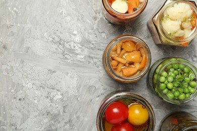 Photo of Different pickled products in jars on grey table, flat lay. Space for text