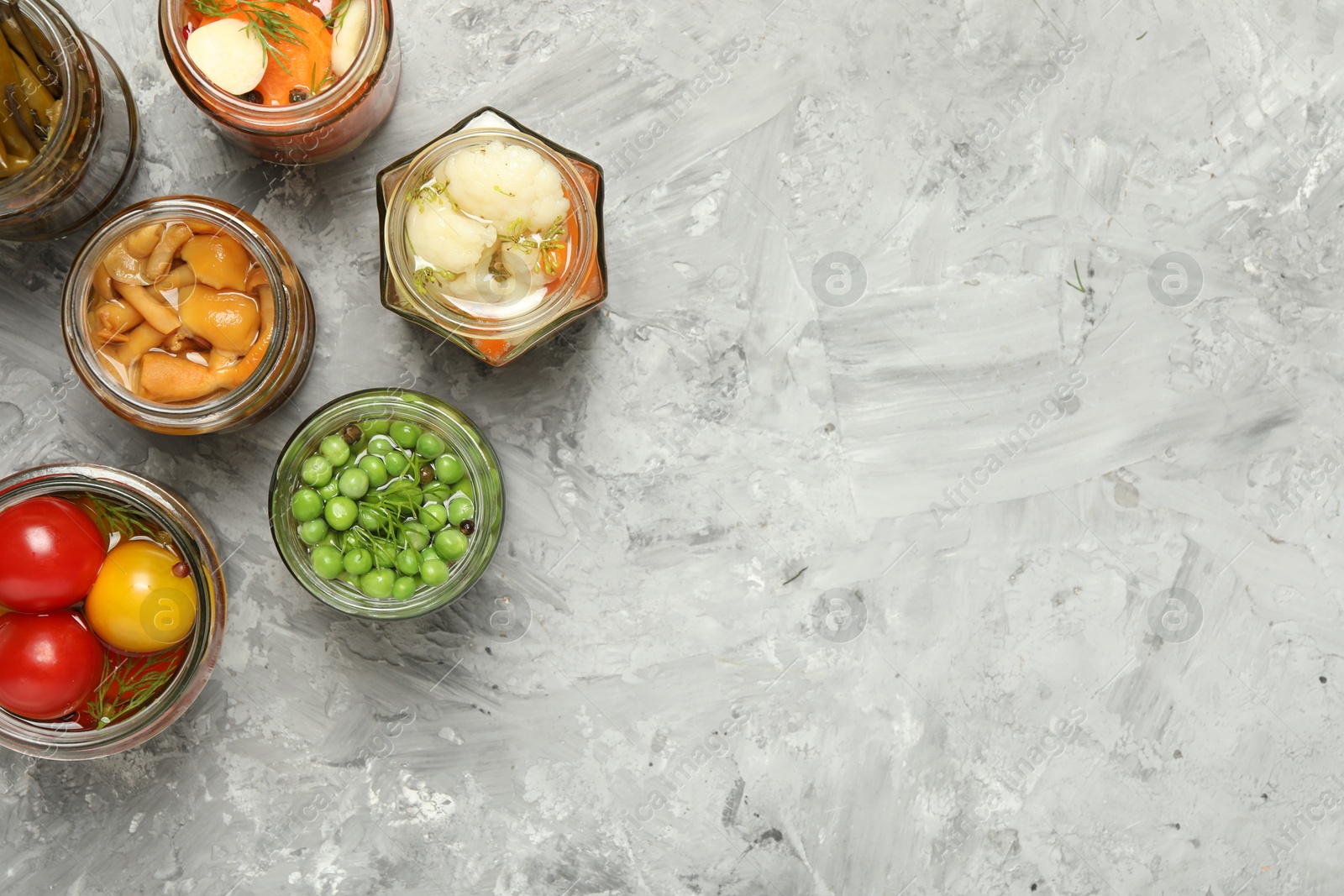 Photo of Different pickled products in jars on grey table, flat lay. Space for text