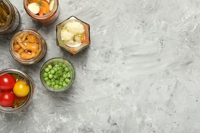 Photo of Different pickled products in jars on grey table, flat lay. Space for text