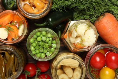 Photo of Different pickled products in jars and fresh ingredients on table, flat lay