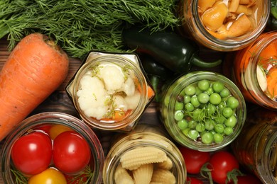 Photo of Different pickled products in jars and fresh ingredients on wooden table, flat lay