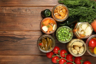 Photo of Different pickled products in jars and fresh ingredients on wooden table, flat lay. Space for text