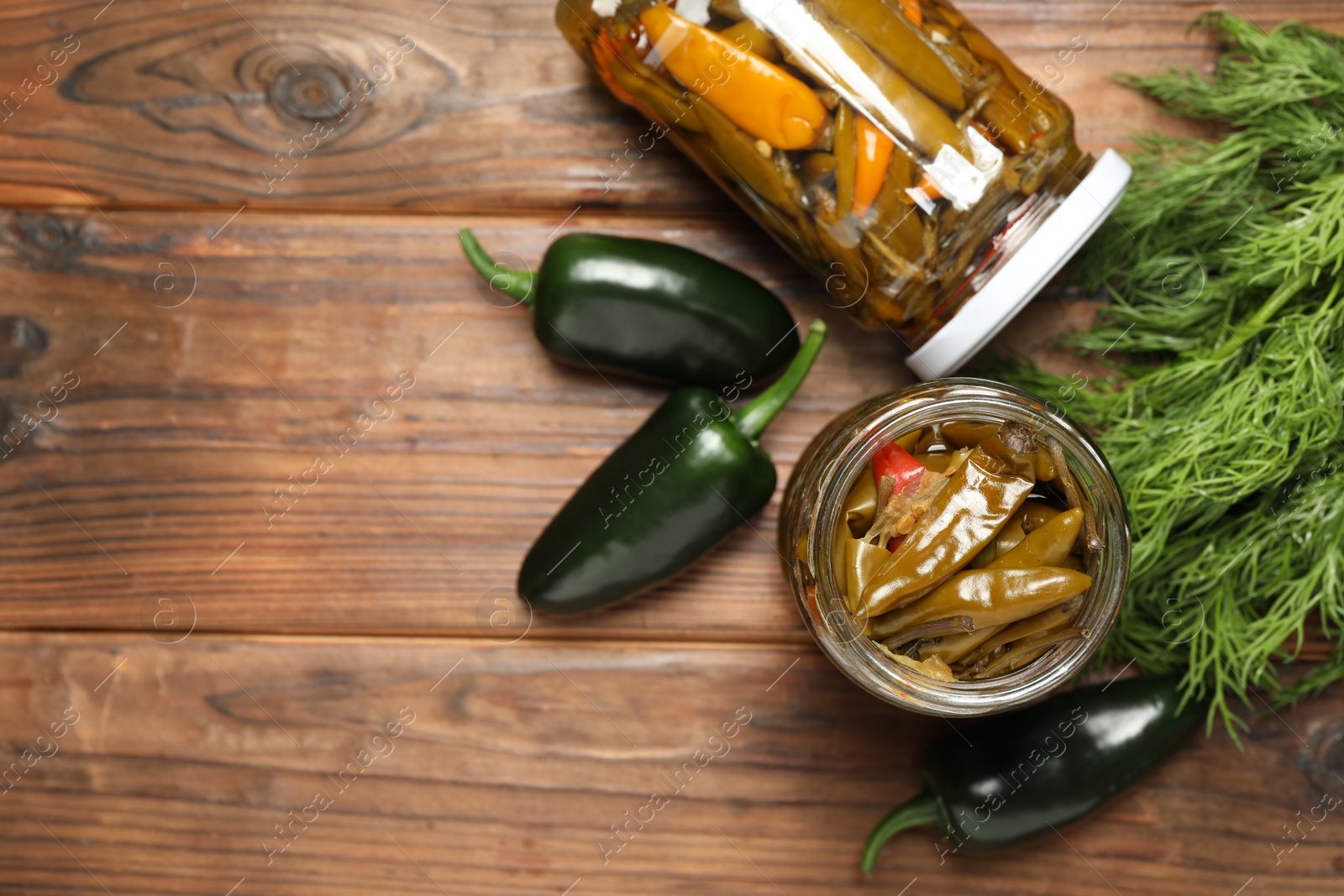 Photo of Tasty pickled jalapeno peppers in jars and fresh ingredients on wooden table, flat lay. Space for text