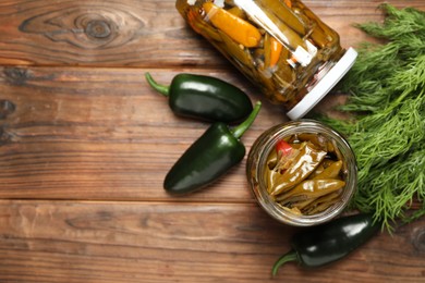 Photo of Tasty pickled jalapeno peppers in jars and fresh ingredients on wooden table, flat lay. Space for text