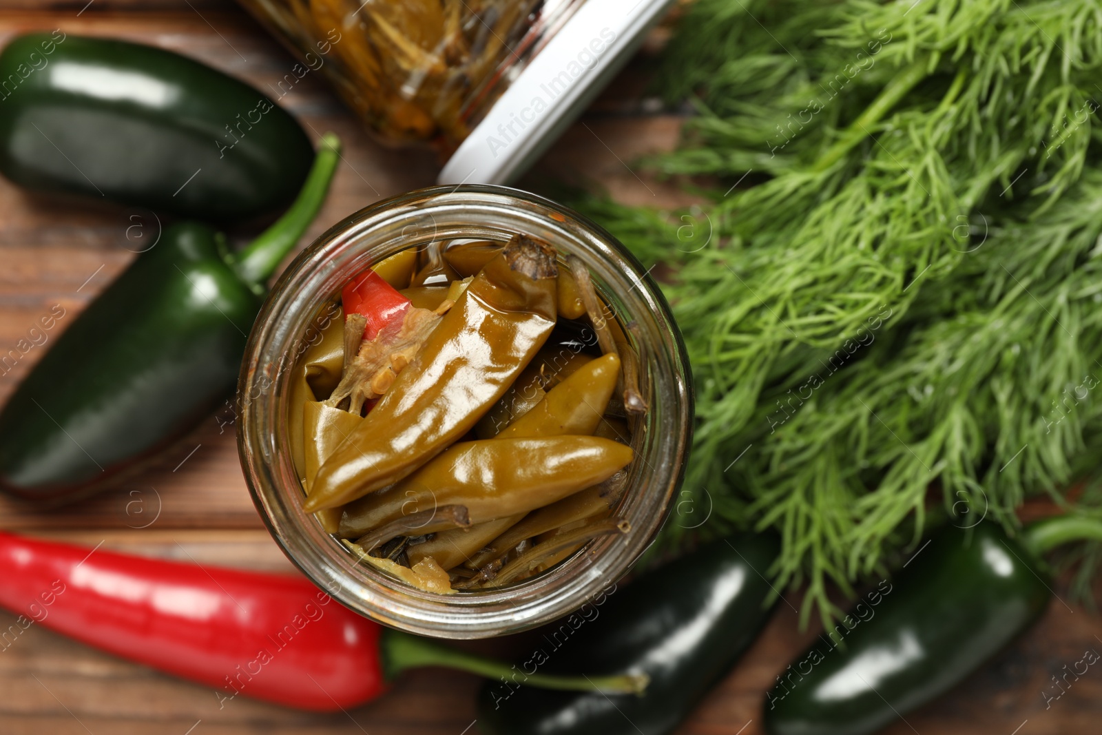 Photo of Tasty pickled jalapeno peppers in jar, fresh vegetables and parsley on table, top view