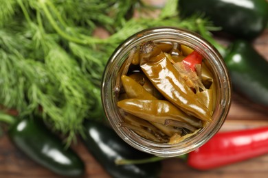 Photo of Tasty pickled jalapeno peppers in jar, fresh vegetables and parsley on table, top view