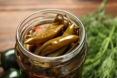 Photo of Tasty pickled jalapeno peppers in jar on table, closeup