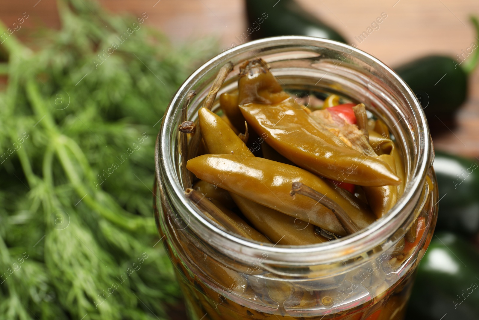 Photo of Tasty pickled jalapeno peppers in jar on table, closeup