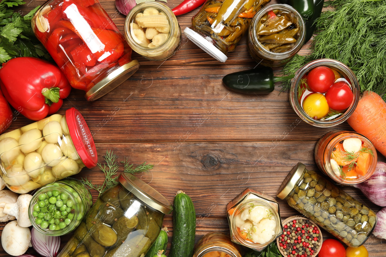 Photo of Frame of different pickled products in jars and fresh ingredients on wooden table, flat lay. Space for text