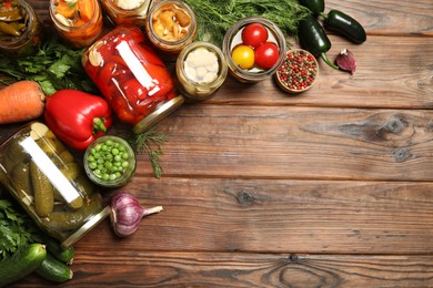 Photo of Different pickled products in jars and fresh ingredients on wooden table, flat lay. Space for text