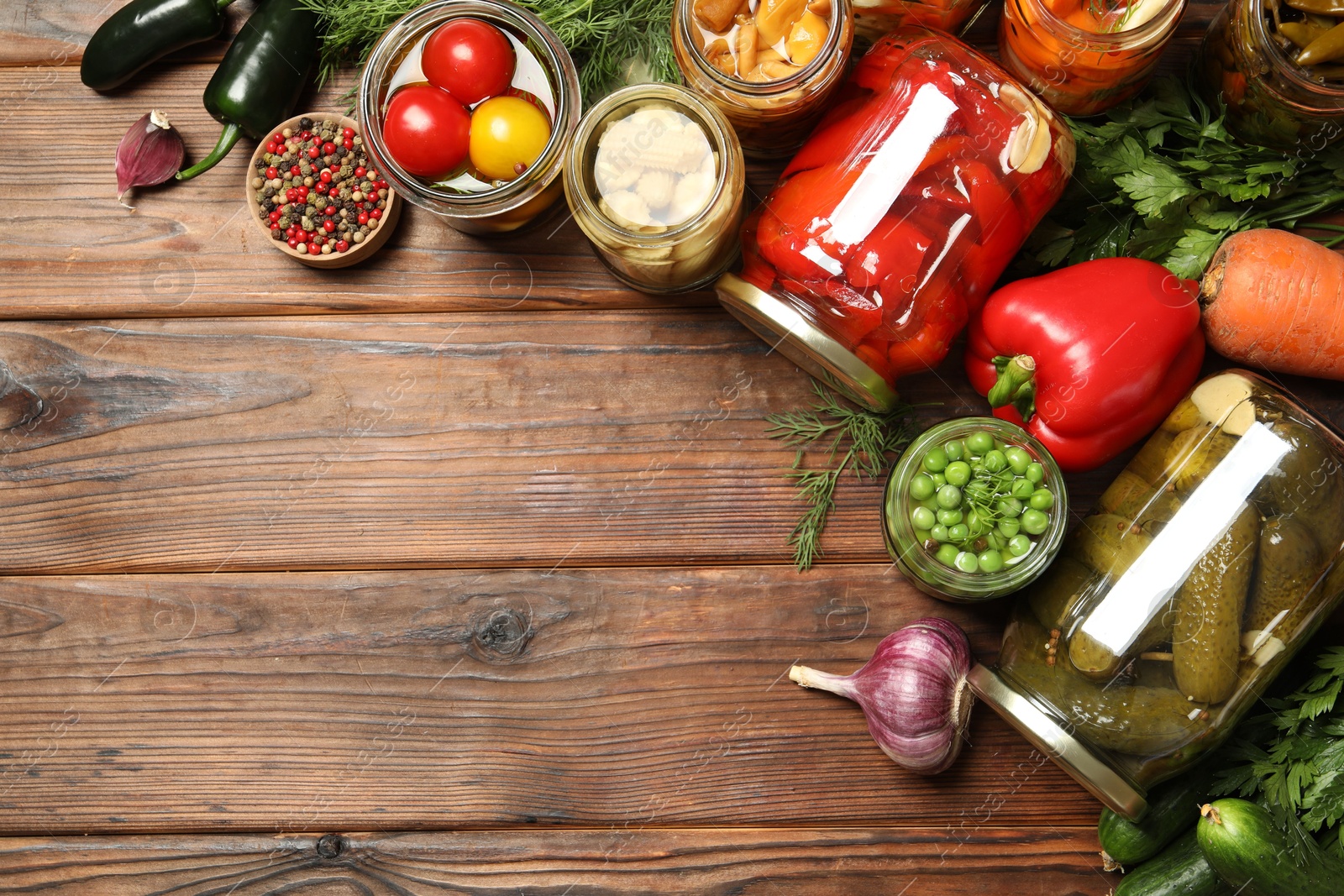 Photo of Different pickled products in jars and fresh ingredients on wooden table, flat lay. Space for text