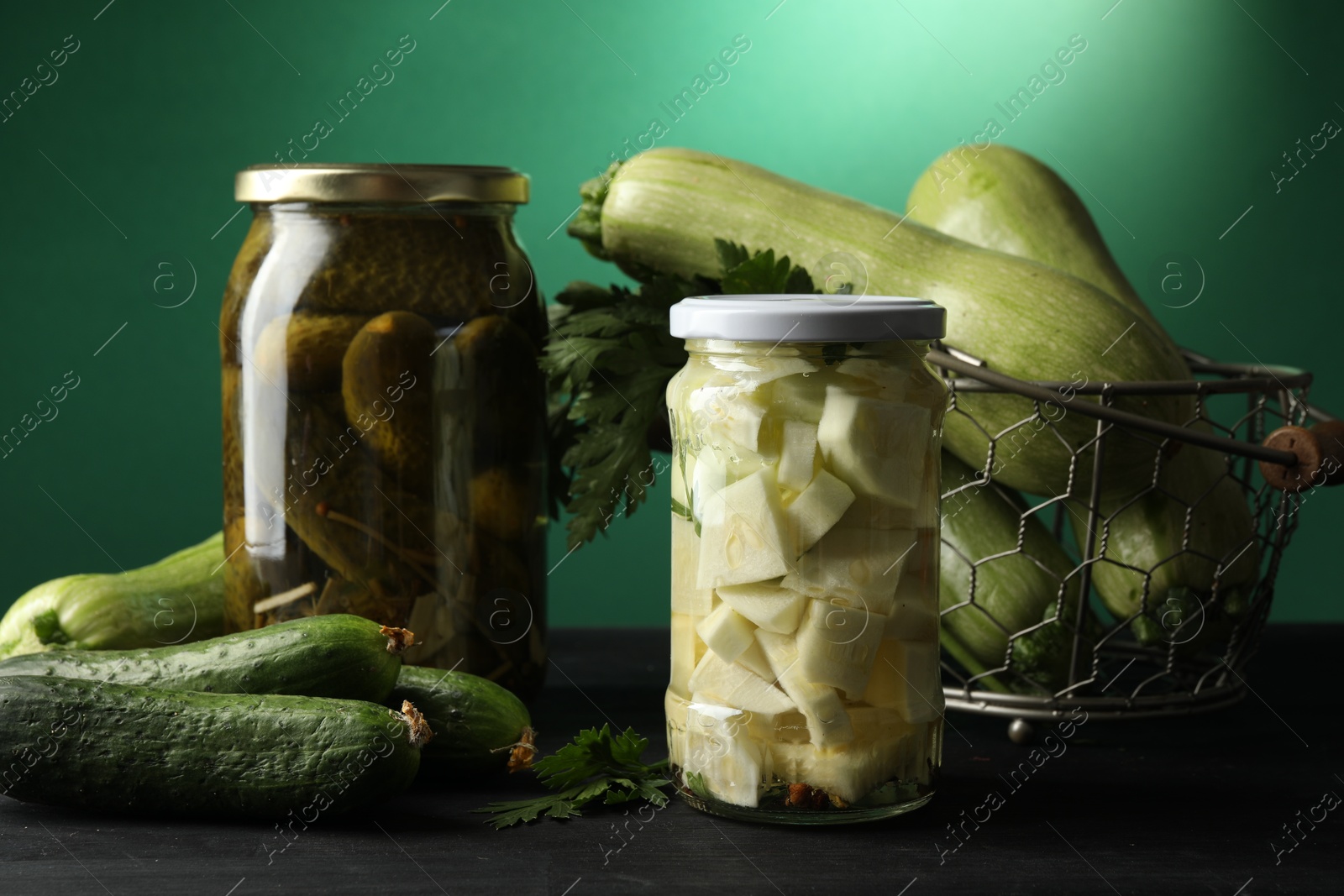 Photo of Different pickled products in jars and fresh ingredients on black wooden table