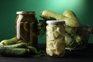 Photo of Different pickled products in jars and fresh ingredients on black wooden table