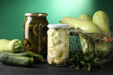 Photo of Different pickled products in jars and fresh ingredients on black wooden table