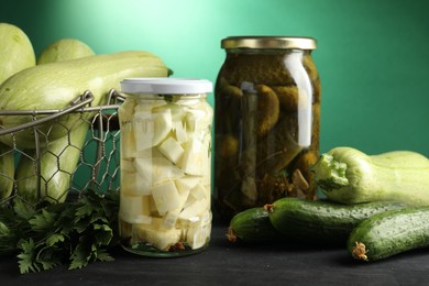 Photo of Different pickled products in jars and fresh ingredients on black wooden table