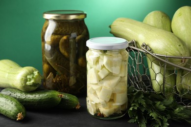 Photo of Different pickled products in jars and fresh ingredients on black wooden table