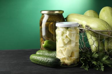 Photo of Different pickled products in jars and fresh ingredients on black wooden table, space for text