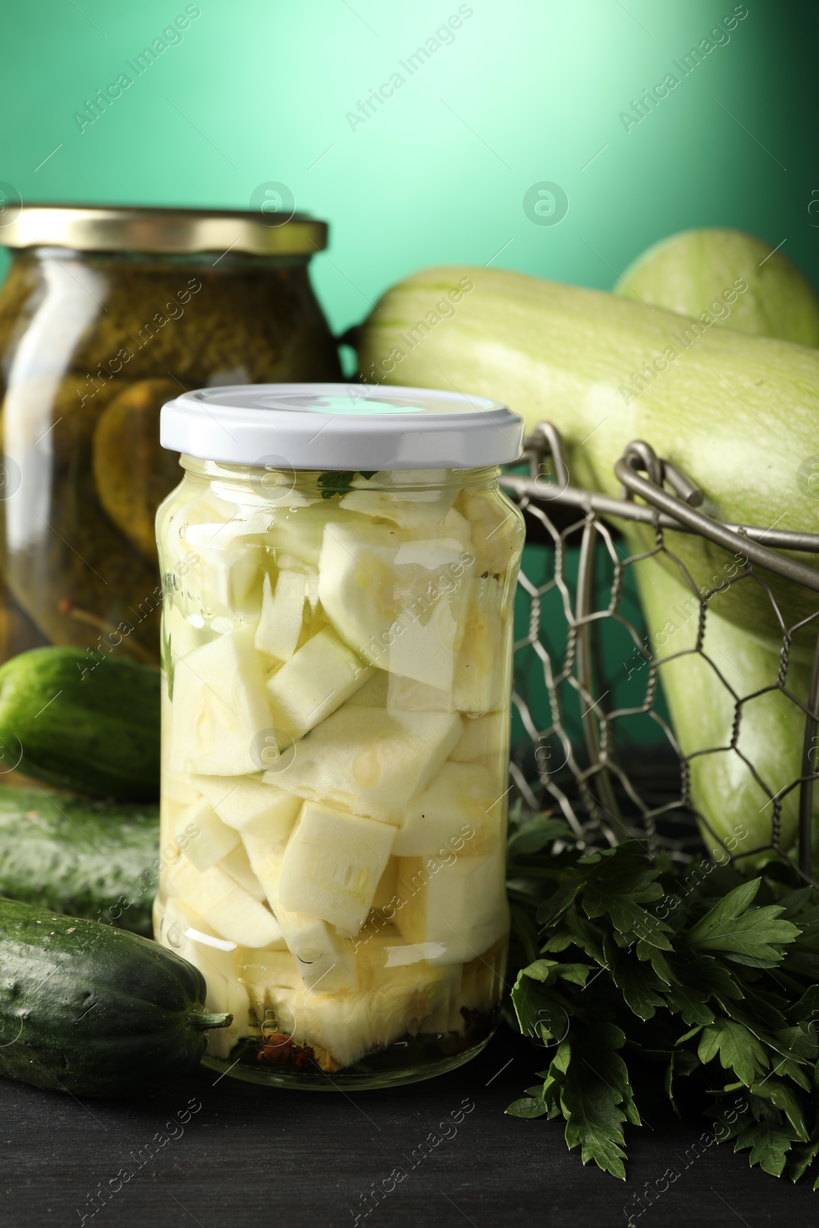 Photo of Different pickled products in jars and fresh ingredients on black wooden table