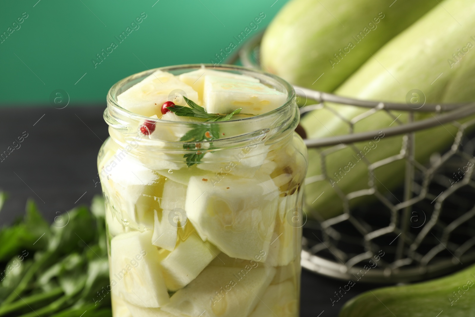 Photo of Tasty pickled zucchini in jar and fresh vegetables on table, closeup