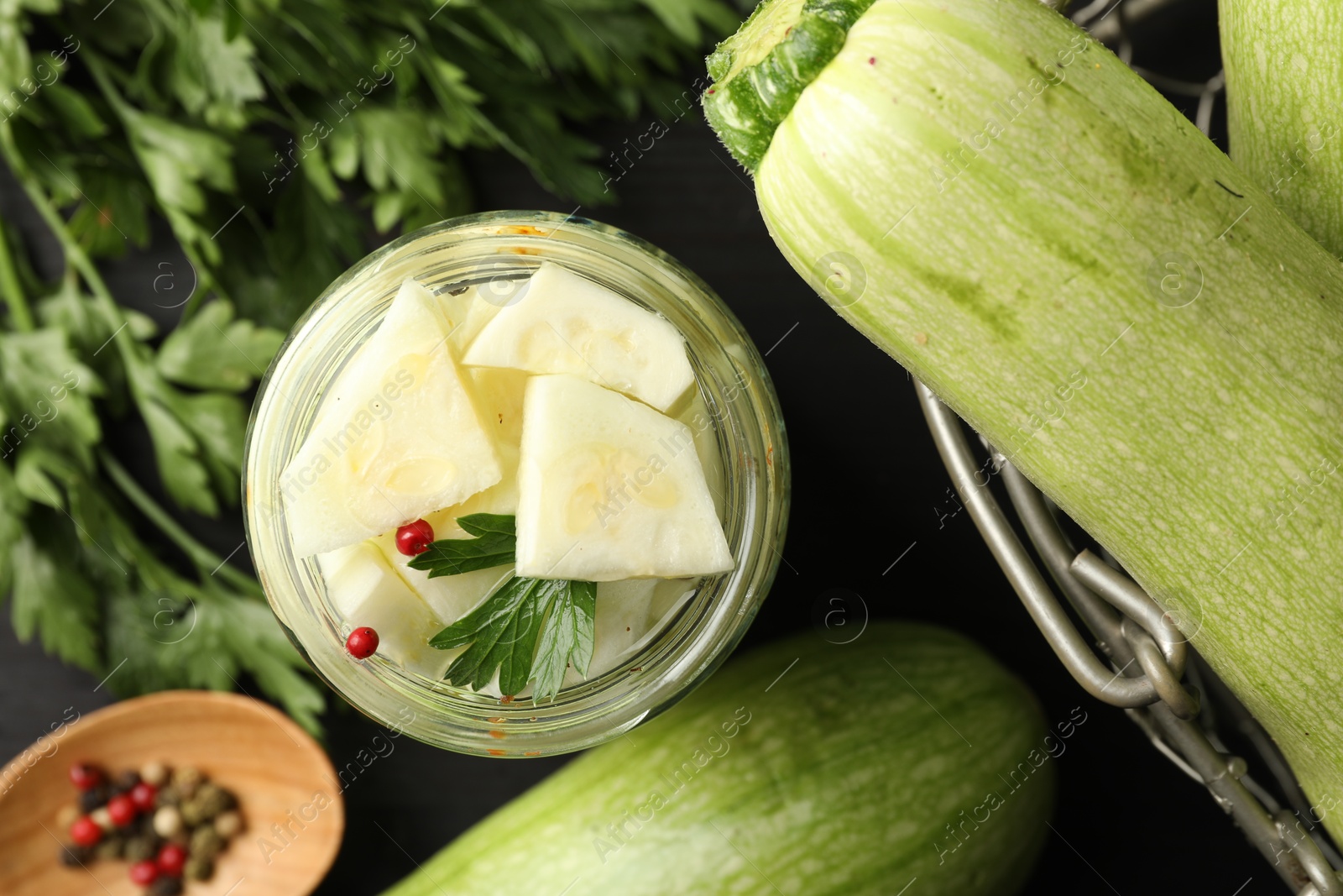 Photo of Tasty pickled zucchini in jar, fresh vegetables, parsley and spices on table, flat lay