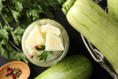 Photo of Tasty pickled zucchini in jar, fresh vegetables, parsley and spices on table, flat lay