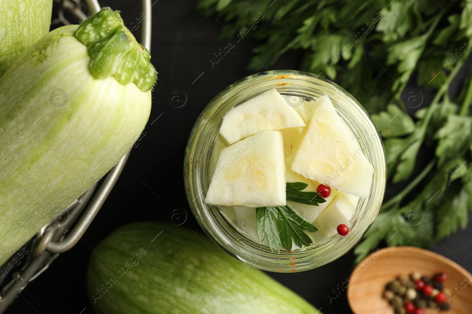 Photo of Tasty pickled zucchini in jar, fresh vegetables, parsley and spices on table, flat lay