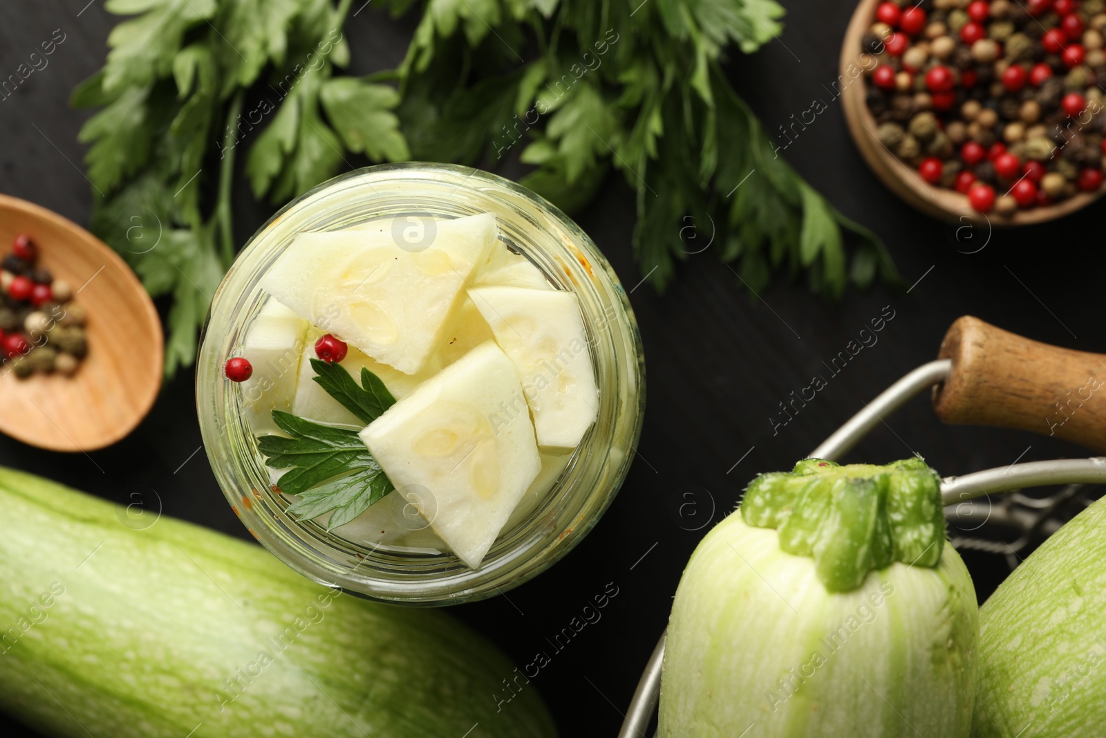 Photo of Tasty pickled zucchini in jar, fresh vegetables, parsley and spices on table, flat lay