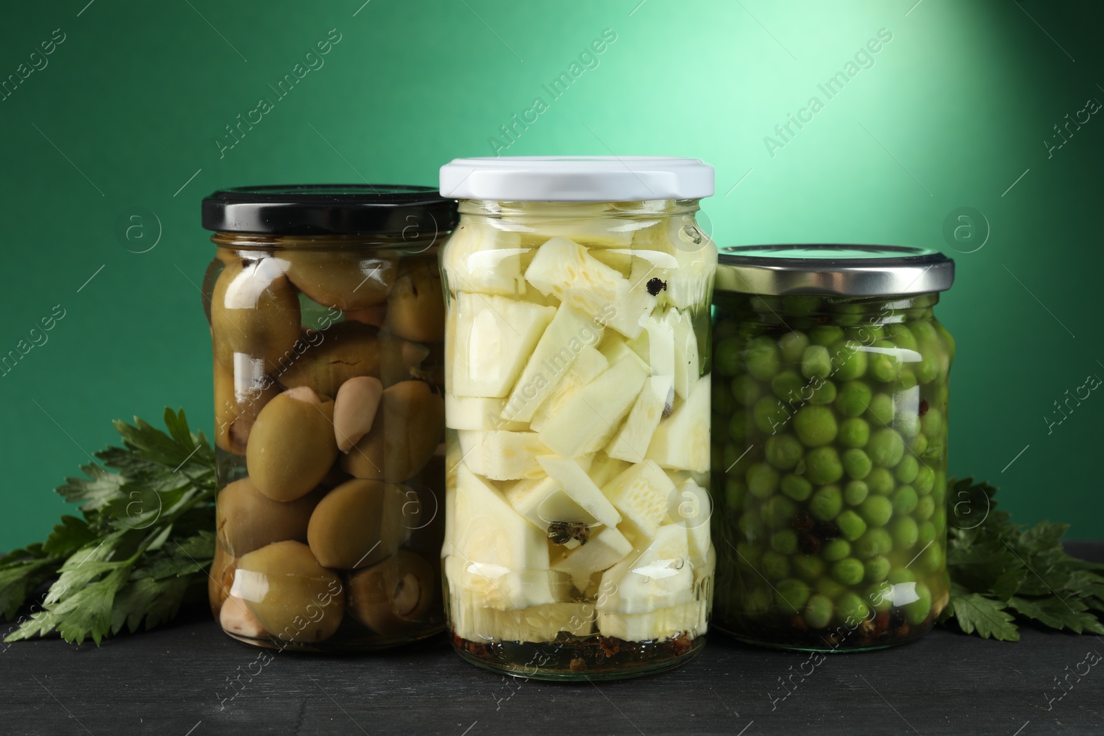 Photo of Different pickled products in jars and parsley on black wooden table