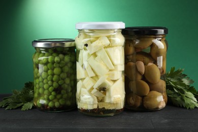 Photo of Different pickled products in jars and parsley on black wooden table