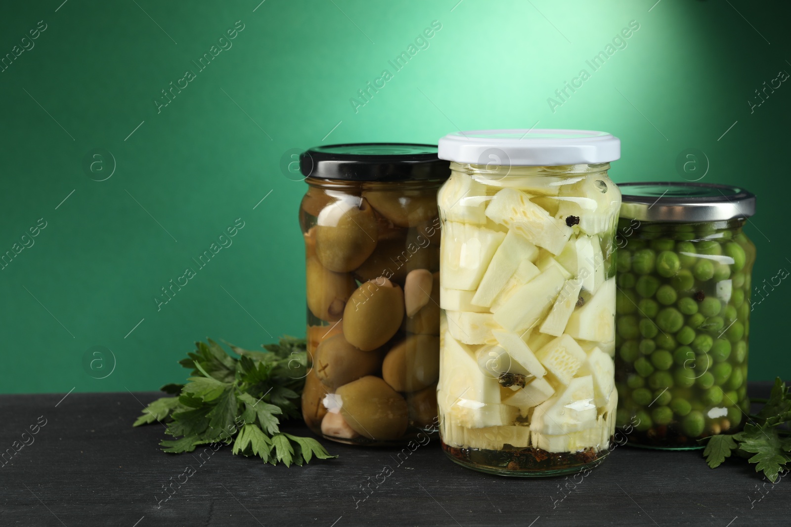 Photo of Different pickled products in jars and parsley on black wooden table