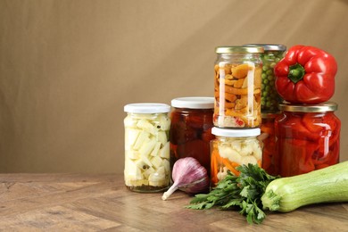 Photo of Different pickled products in jars and fresh ingredients on wooden table, space for text