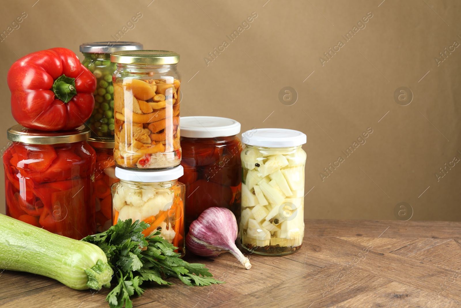 Photo of Different pickled products in jars and fresh ingredients on wooden table, space for text