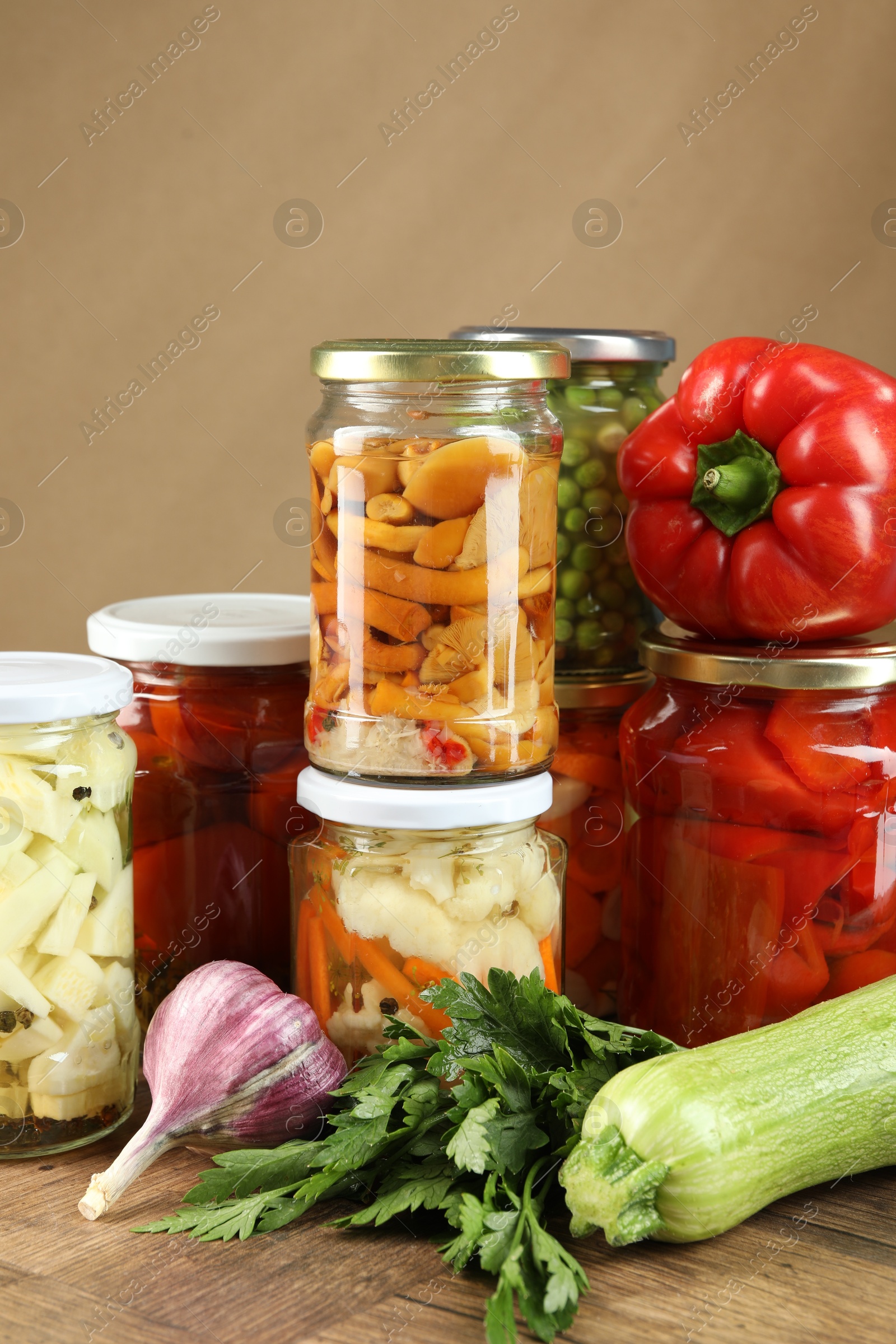 Photo of Different pickled products in jars and fresh ingredients on wooden table