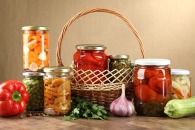 Photo of Different pickled products in jars and fresh ingredients on wooden table