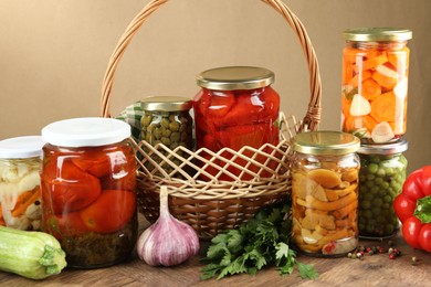 Photo of Different pickled products in jars and fresh ingredients on wooden table