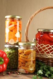 Photo of Different pickled products in jars and fresh ingredients on wooden table