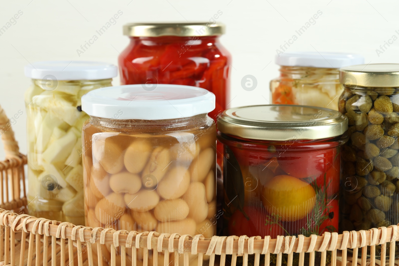 Photo of Different pickled products in jars in wicker basket, closeup