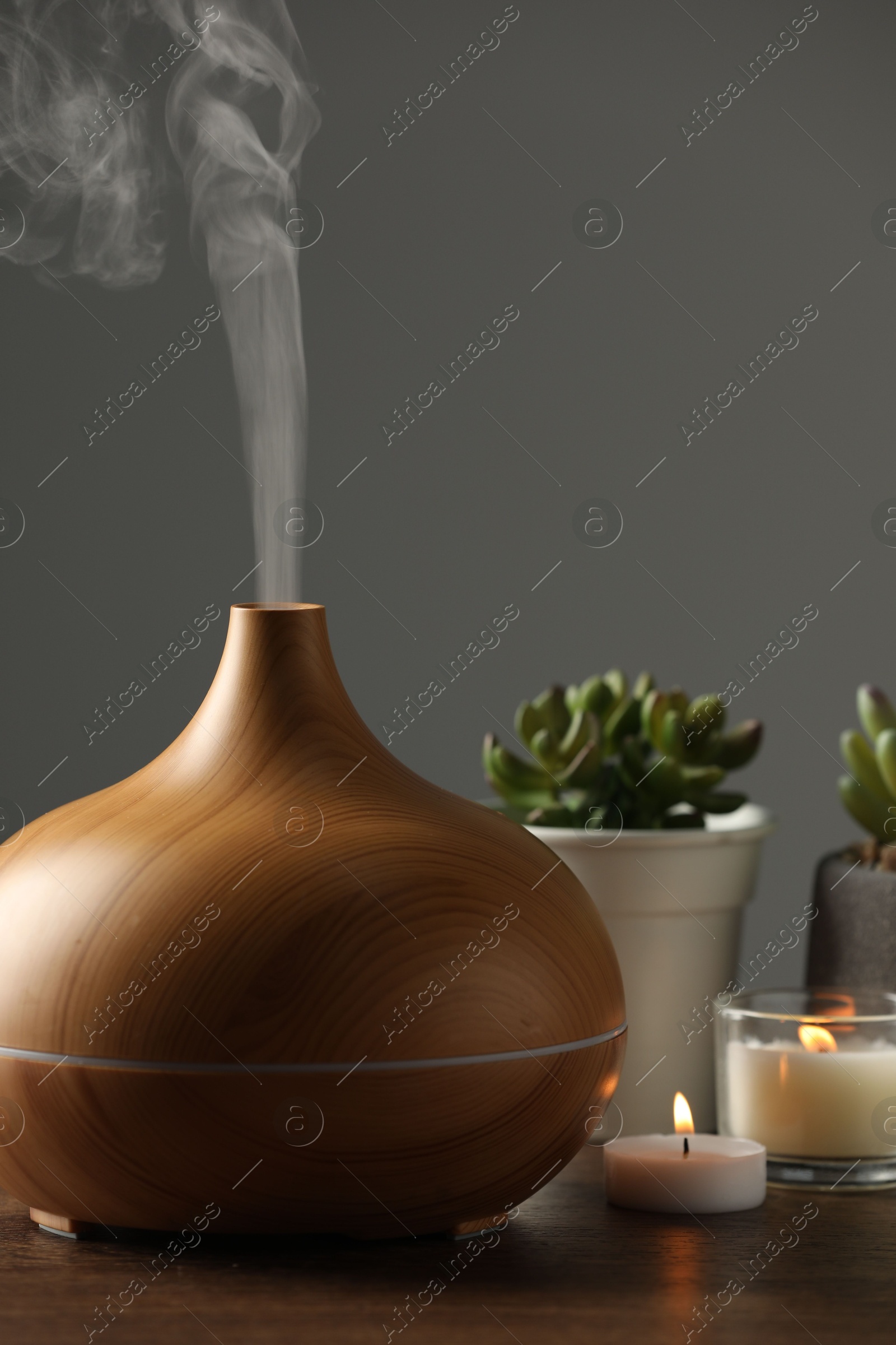 Photo of Aroma oil diffuser, houseplants and burning candles on wooden table