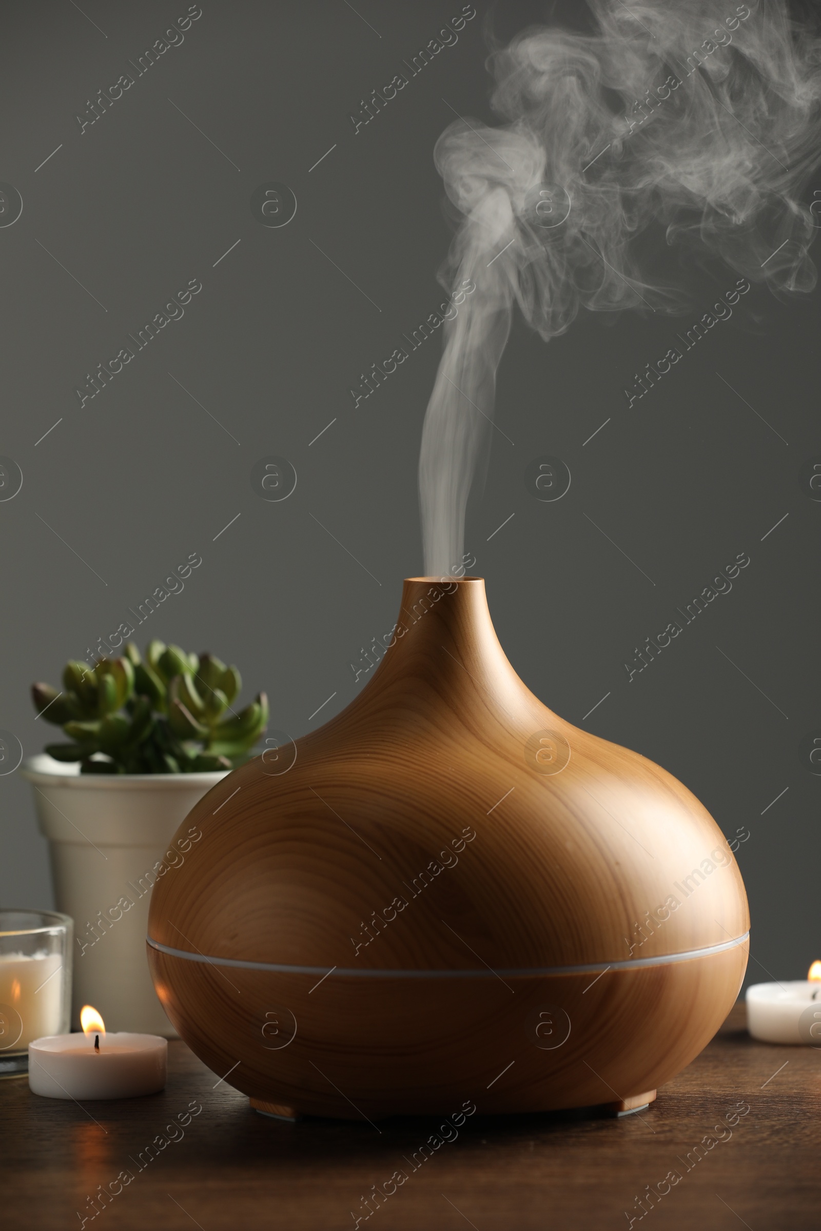 Photo of Aroma oil diffuser, houseplants and burning candles on wooden table