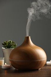 Aroma oil diffuser, houseplants and burning candles on wooden table