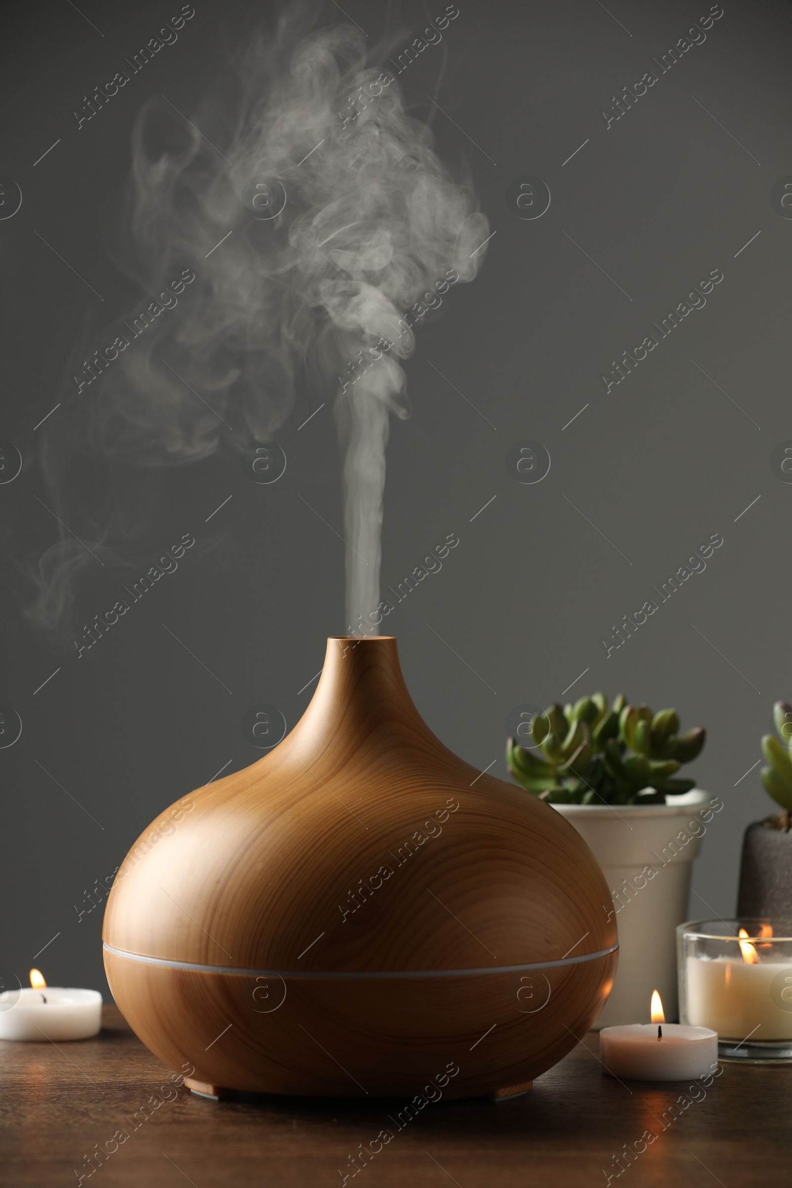 Photo of Aroma oil diffuser, houseplants and burning candles on wooden table