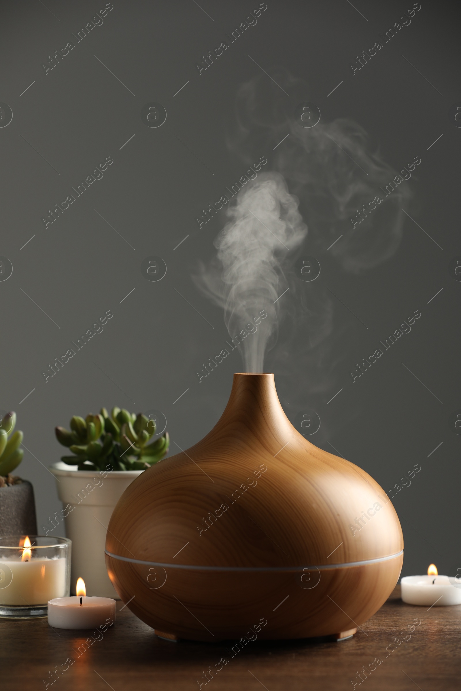 Photo of Aroma oil diffuser, houseplants and burning candles on wooden table