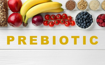 Image of Word Prebiotic and different gut-healthy foods on white wooden table, top view